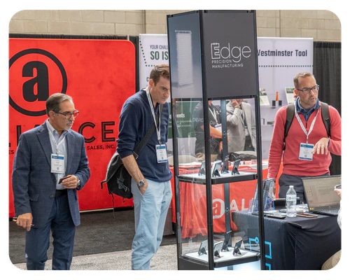 Three men standing by a table at a trade show, exploring innovations and networking with attendees.