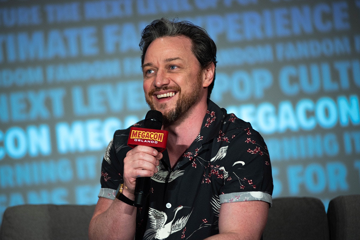 James McAvoy smiles wearing a hawaiian shirt & holding a microphone