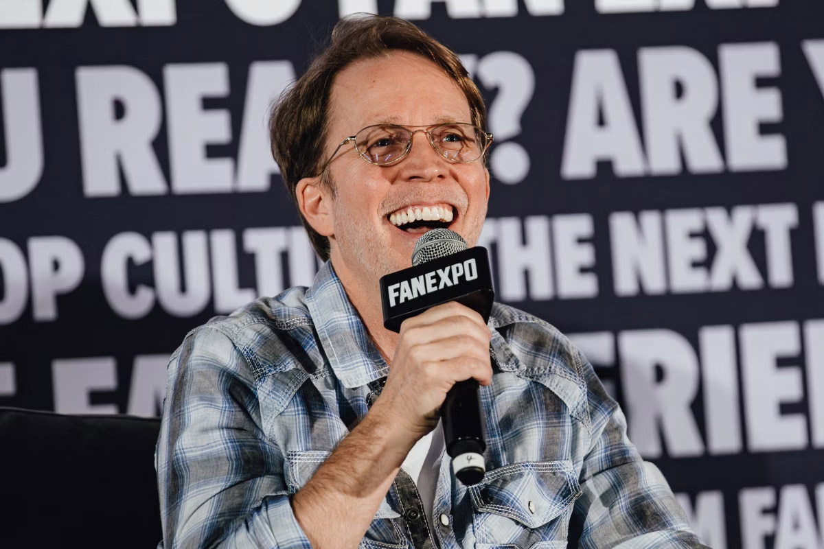 James Arnold Taylor smiles on stage holding a microphone