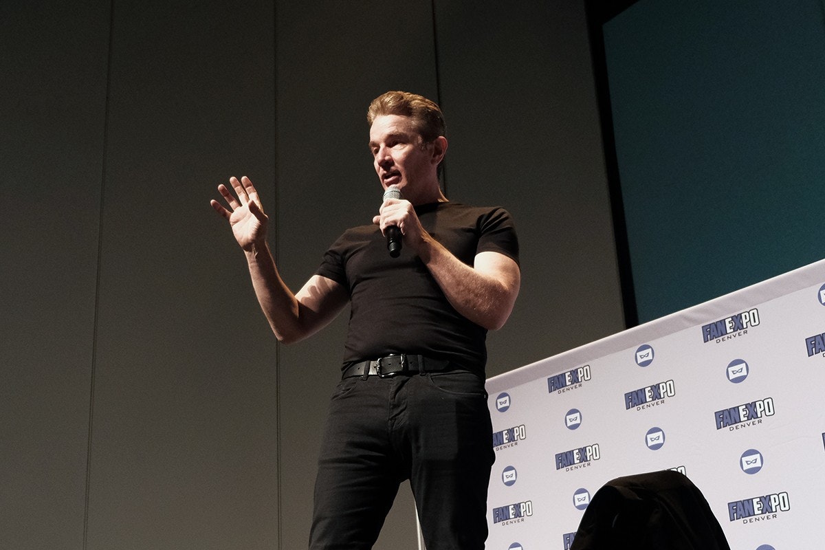 James Marsters looks serious with a hand extended as he speaks into a microphone