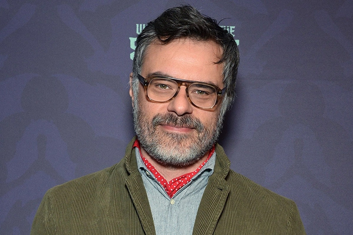 Jermaine Clement smiles for a photo with a green jacket and brown glasses on