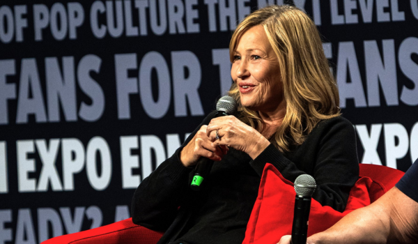 Andy is sitting in a black chair on stage. He is wearing a black leather jacket with a black and red t-shirt underneath.