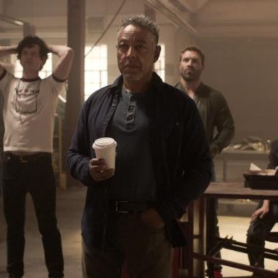 Giancarlo holding a white coffee cup looking at something intensely. There is also a guy in a white shirt with his hands over his head and another guy directly to his right looking intimidating.