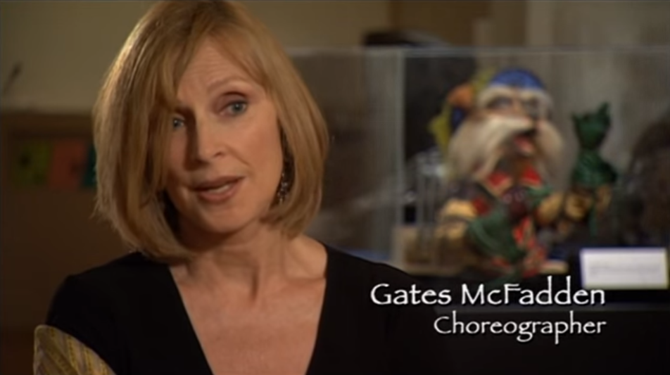 Gates McFadden with short hair and black top/ Behind her is Sir Didymus from the Labyrinth. Caption: Gates McFadden Choreographer