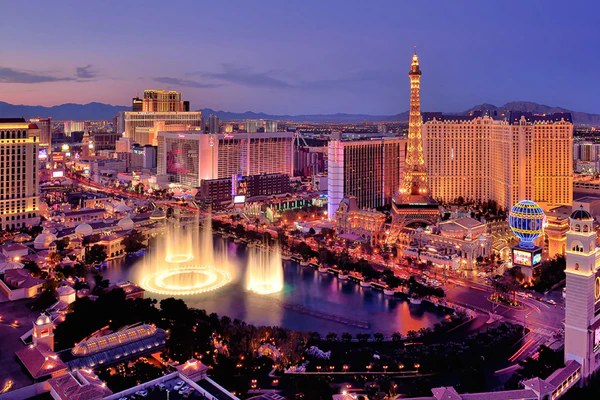 Evening view of the Las Vegas Strip featuring the Bellagio Fountains, the Paris Las Vegas Eiffel Tower and hot air balloon, and surrounding resort lights, showcasing the vibrant attractions near HDI Service & Support World at Caesars Palace.
