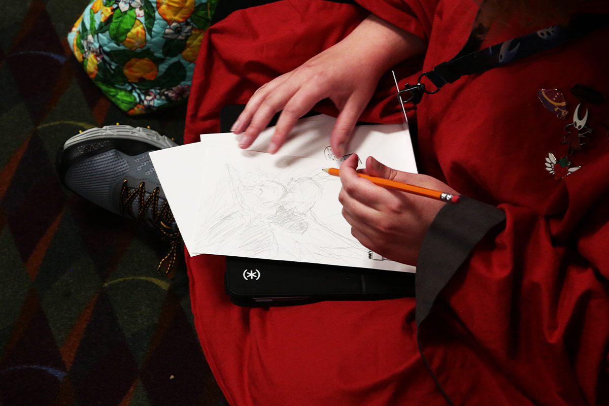 A cosplayer in red draws on a piece of paper with a pencil