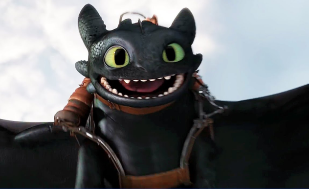 A back dragon, with blunted teeth and a brown harness flies through the sky with a wide smile.