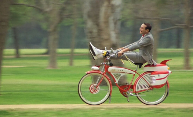Pee-wee whizzes through the park on his cherry red big wheel, his legs kicked up over the handle bars.