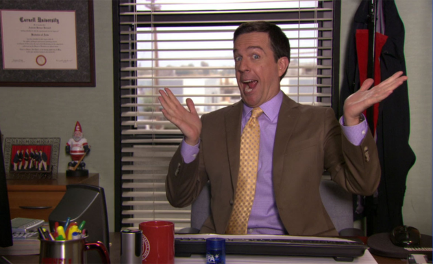 Andy, seated behind his desk, smiling with his mouth open and hands out-stretched in an excited manner.