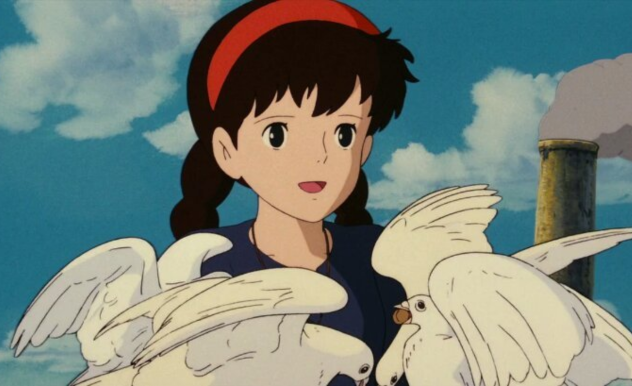 Sheeta feeds a group of white doves and smiles as they eat the bread she provides. 