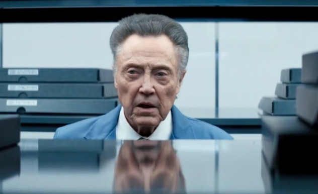 Staring through the shelves, mid-sentence, Burt is framed by boxed up art with small white labels