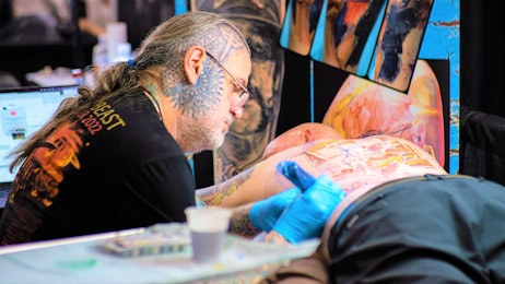 A tattoo artist is giving a fan a back tattoo