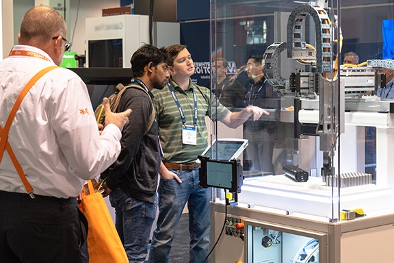 A group of people observes a machine on display at an exhibition, engaged in discussion about its features