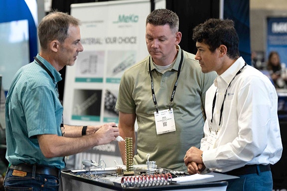 Three men engaged in conversation at a trade show table, discussing products and networking with attendees