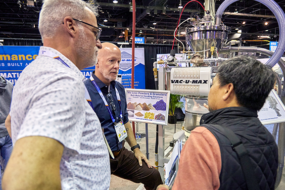 Exhibitor in a black shirt showcasing a machine to two interested attendees