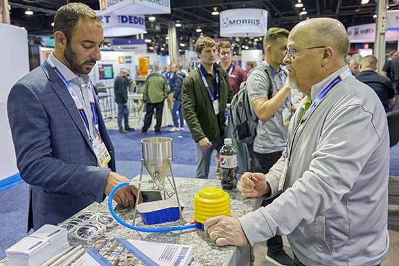 Two men stand by a table, examining a yellow object placed in front of them