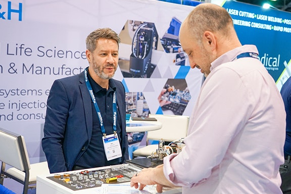 Two men engaged in conversation at a trade show, surrounded by booths and attendees