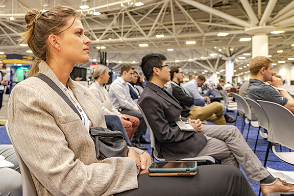 A woman seated in a big conference hall listening a conference presentation