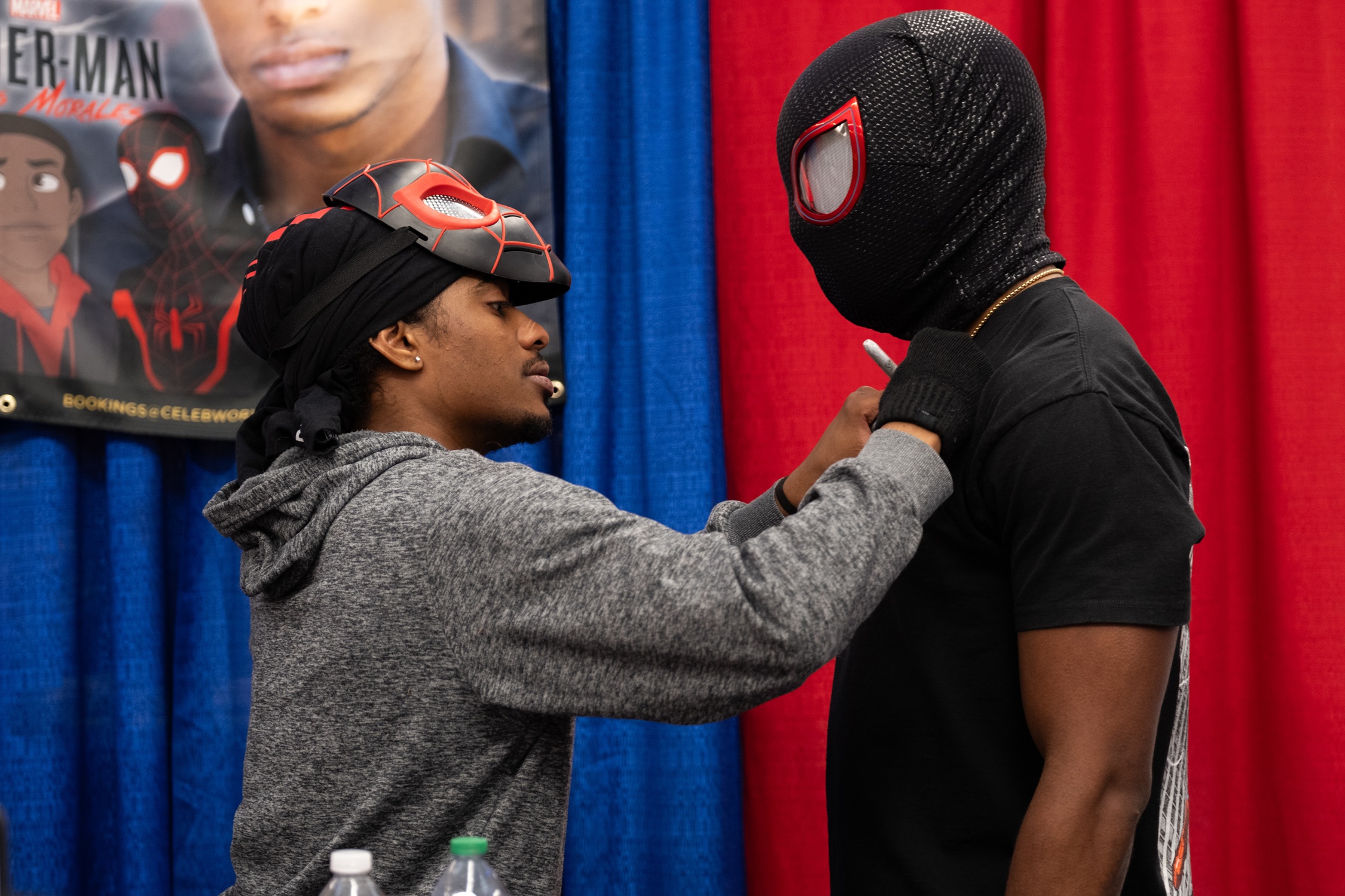 Voice actor Nadji Jeter signs the chest of a fan dressed as Spider-Man: Miles Morales. A banner showing the animated character version of Miles is displayed behind them.