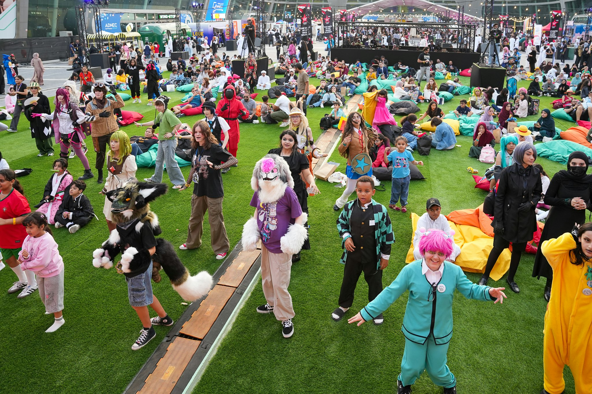 Cosplayers and fans cheer during an outdoor activity challenge at MEFCC Festival Plaza, surrounded by a lively Comic Con crowd.