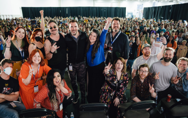 The full voice actor cast of My Hero Academia smiling and posing on the main stage, with the audience in the background.