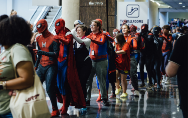 A conga line of dozens of Spider-Man cosplayers dancing through the convention center lobby.