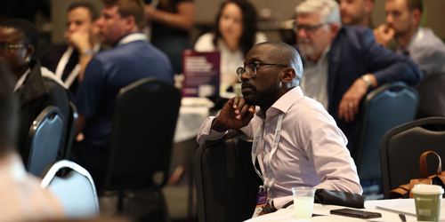 A man sits in a crowded audience listening to a session at MSP Summit.
