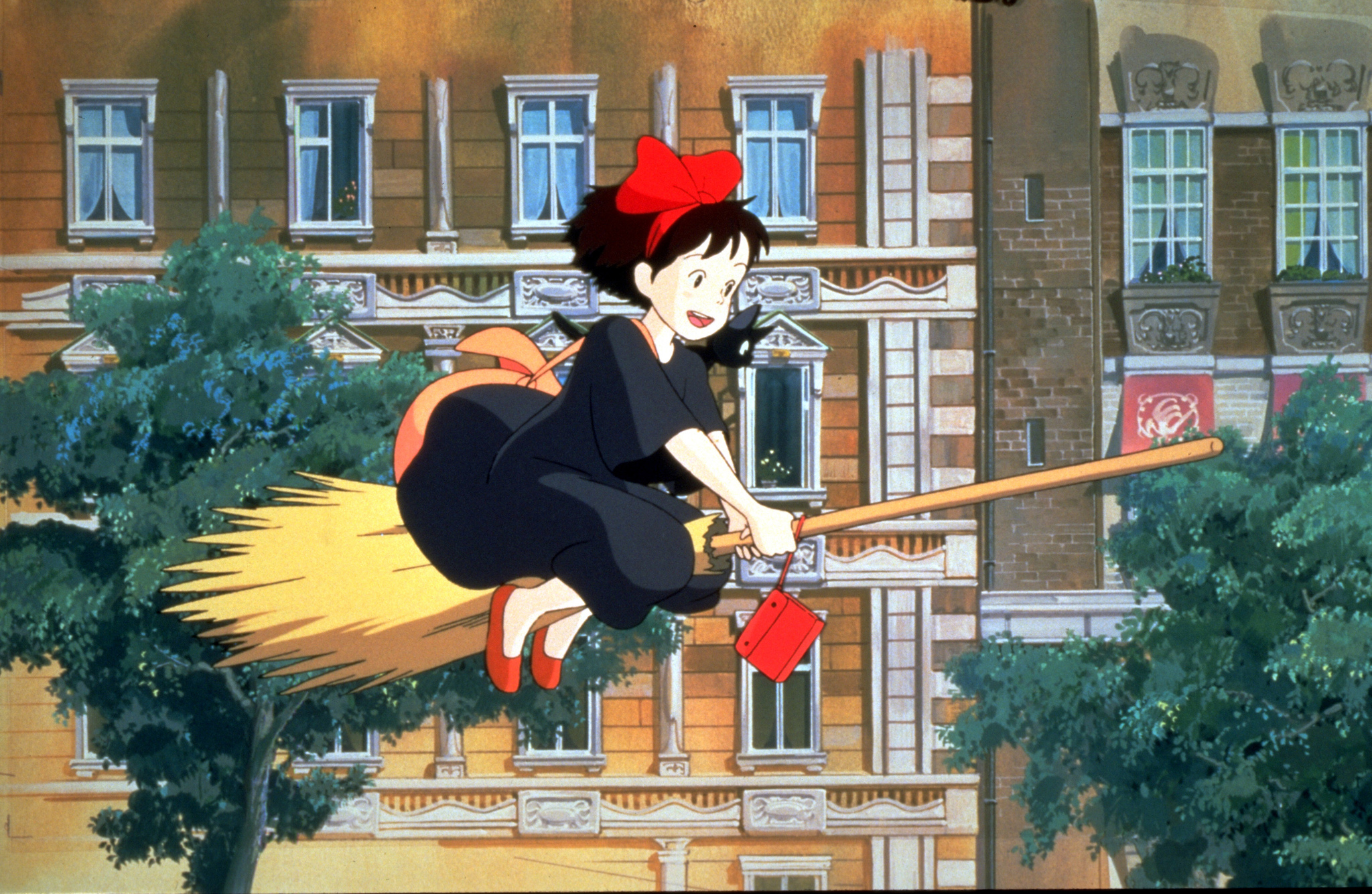 Kiki and Jiji fly over the city. Jiji sits on Kiki's shoulder as they move.