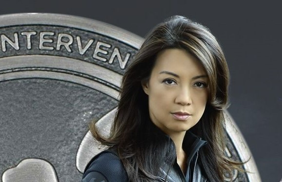 Ming-Na Wen as Professor Melinda Qiaolian May. She is wearing a dark Shield's uniform and behind her is the silver/gray crest of shield. The only letters showing are "NTERVEN"