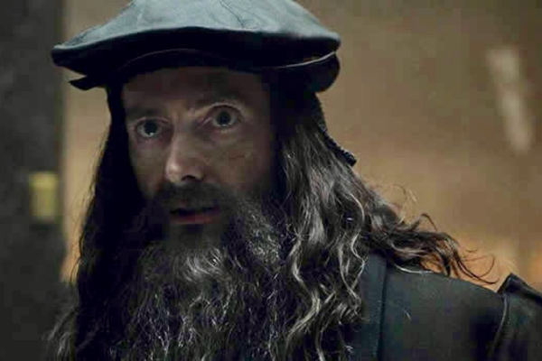 David Tennant is in dark clothing and has long hair, long beard and a black cap