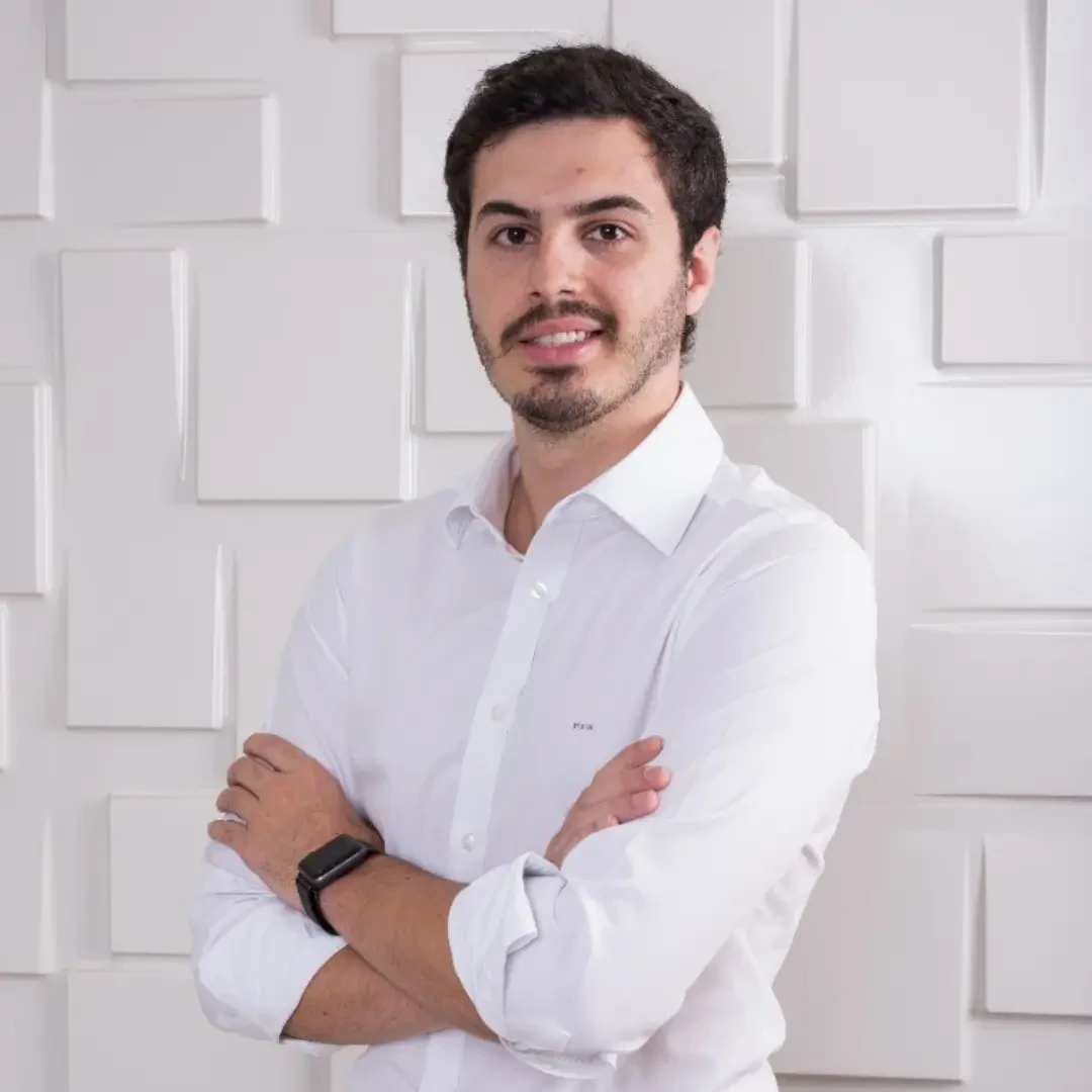 Matheus Prado Nascimento, palestrante de saúde, de camisa branca e braços cruzados sobre fundo claro.
