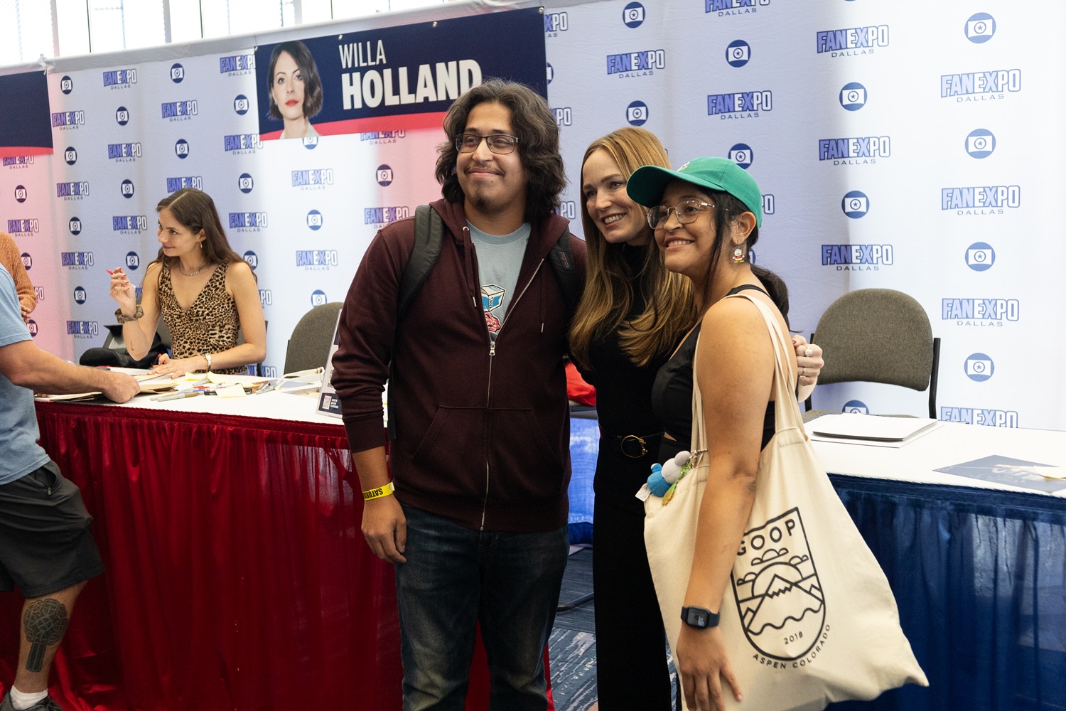 Caity Lotz poses with two fans in front of her autograph station at Dallas FAN FESTIVAL.