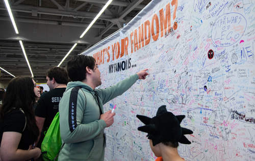 Fans pointing at and signing a "What's your fandom?" Banner