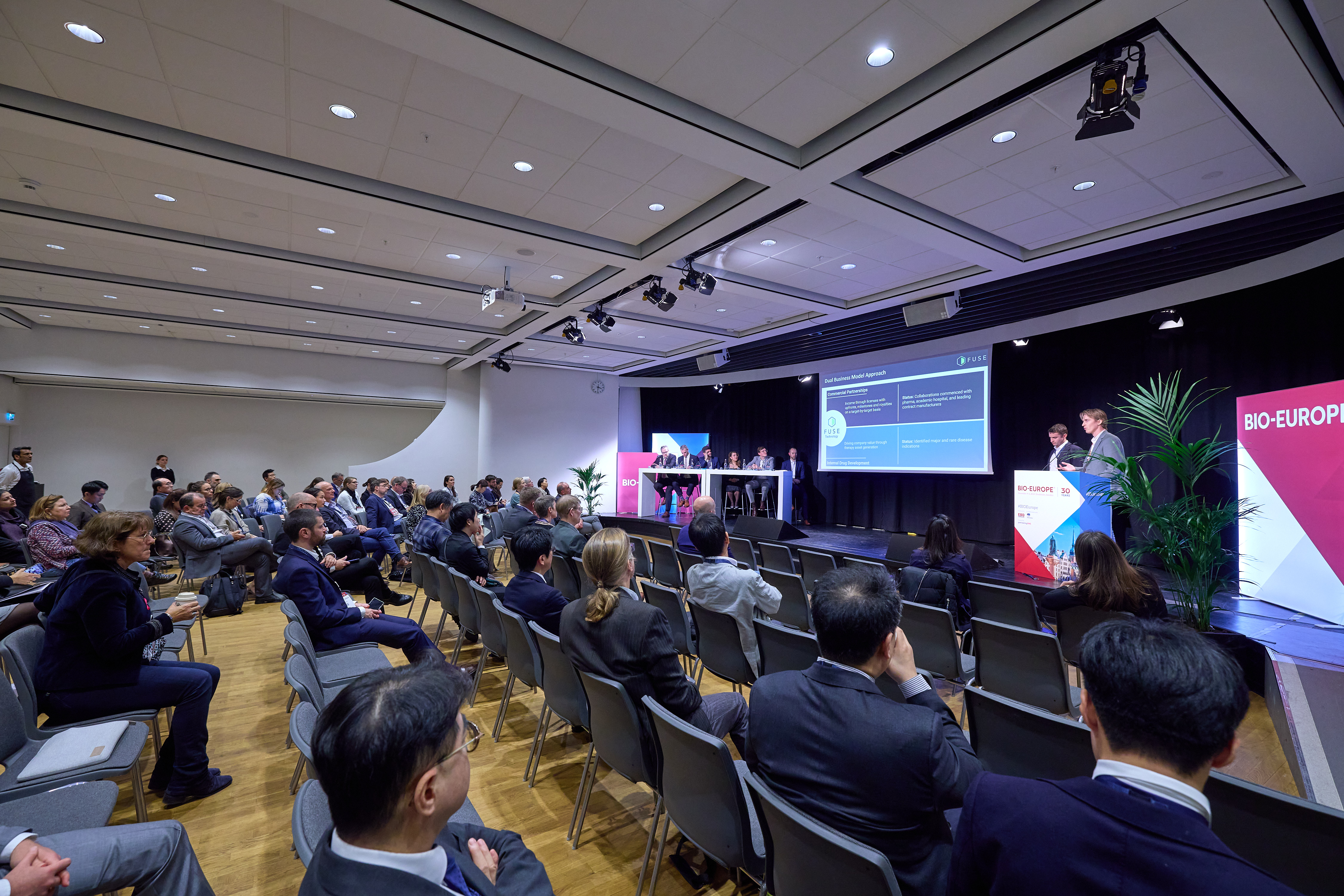 a view from the back of the presenting room with a crowd and presenter
