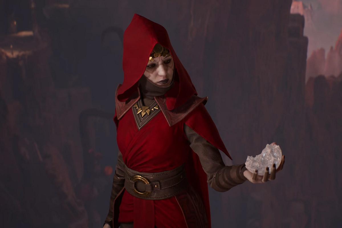 Merrin, a Nightsister in a red outfit, stands holding a broken glass orb while looking at it sadly
