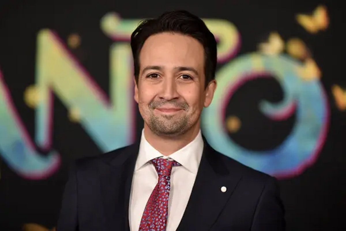 Lin-Manuel Miranda smiles in front of an Encanto backdrop