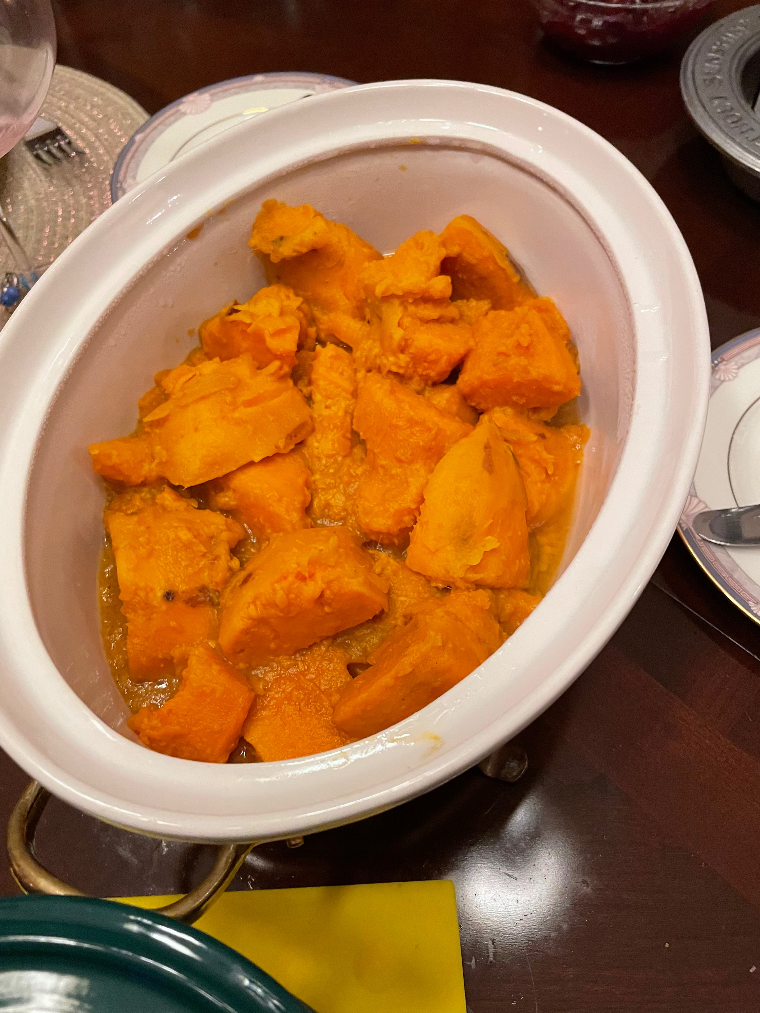 Orange yams are in a white oval shaped bowl on top of a brown table
