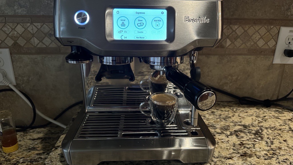 A silver Breville espresso machine sits on top of a granite counter top.