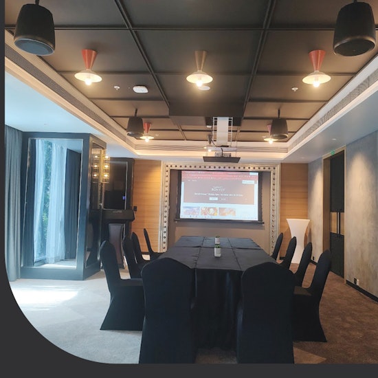 Modern conference room with a central table covered in black cloth, surrounded by chairs, and a large projection screen at the front