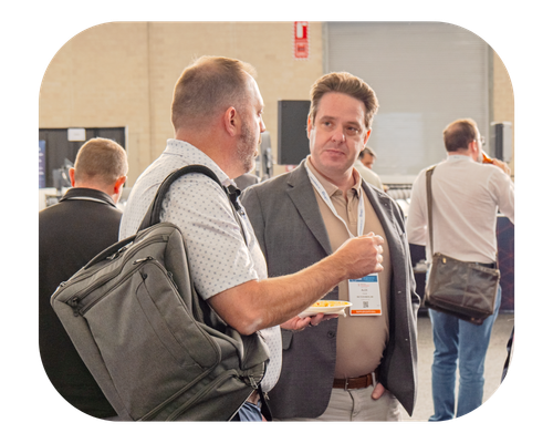 A man carrying a backpack talks with an attendee, sharing ideas at a gathering