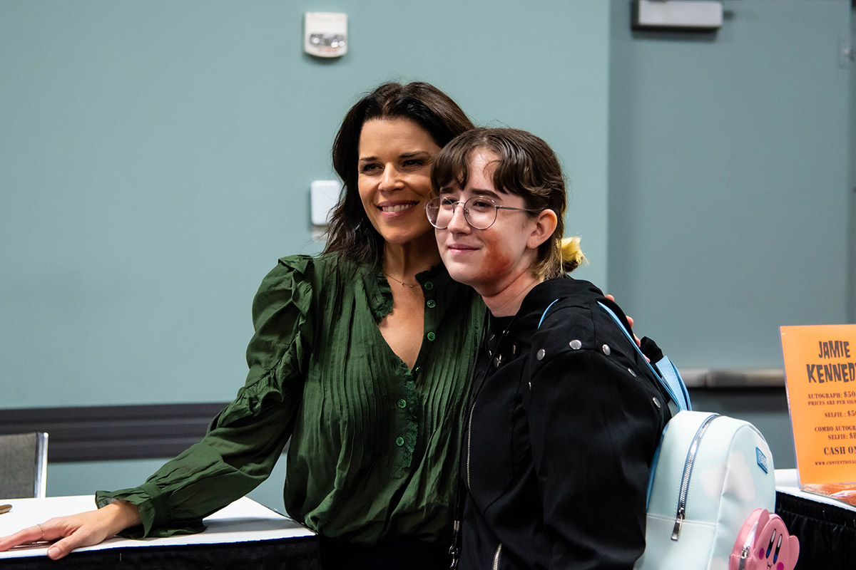 Neve Campbell smiles next to a fan while wearing a green frilly shirt
