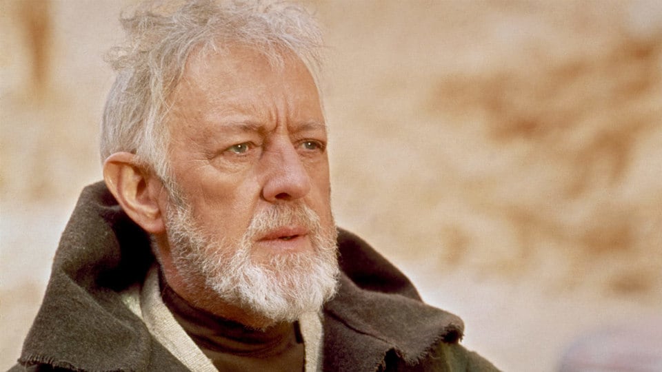 Older Obi-Wan from Star Wars stands with scruffy beard and brown robes