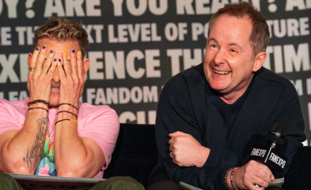 The image captures a humorous moment during a panel at FAN EXPO. Dominic Monaghan and Billy Boyd are depicted, Dominic with his face covered by his hands, showing colorful nail polish, and Billy laughing joyfully while holding a microphone. Billy is dressed in a dark navy sweater, clearly enjoying Dominic's reaction or the audience's. Their playful and relaxed demeanor highlights the lively and interactive nature of the panel. The backdrop is filled with phrases about fandom and pop culture, enhancing the fan-focused atmosphere of the event.