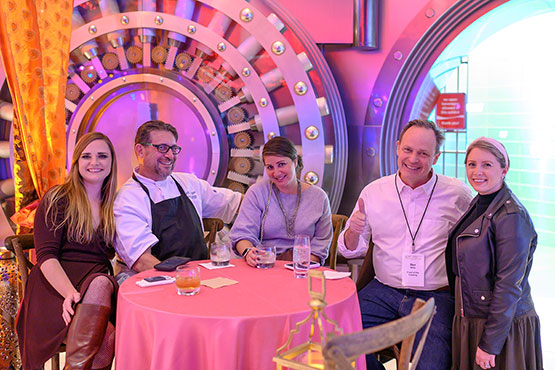 A diverse group of individuals sitting at a table in front of a large machine, engaged in a meeting.