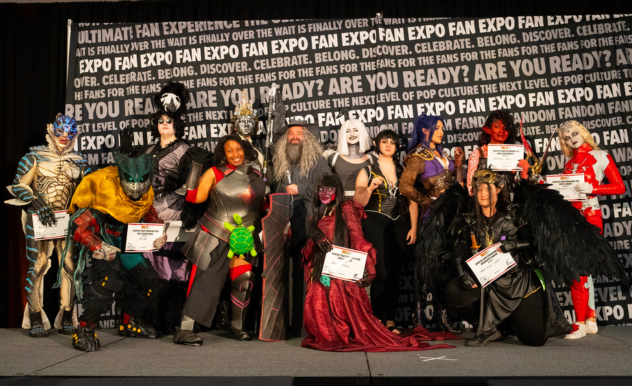 The image captures a diverse group of cosplayers at FAN EXPO, all winners in a costume competition, showcasing their creativity and craftsmanship. The group includes a wide array of characters, from fantastical creatures with elaborate body suits and makeup to heroes and villains in detailed armor and robes. Each cosplayer holds a certificate, signifying their achievement. The variety of costumes displays an impressive range of materials and designs, reflecting the individuality and passion of the cosplay community. The backdrop filled with text promoting the expo sets the stage for this celebration of fandom and artistic expression.
