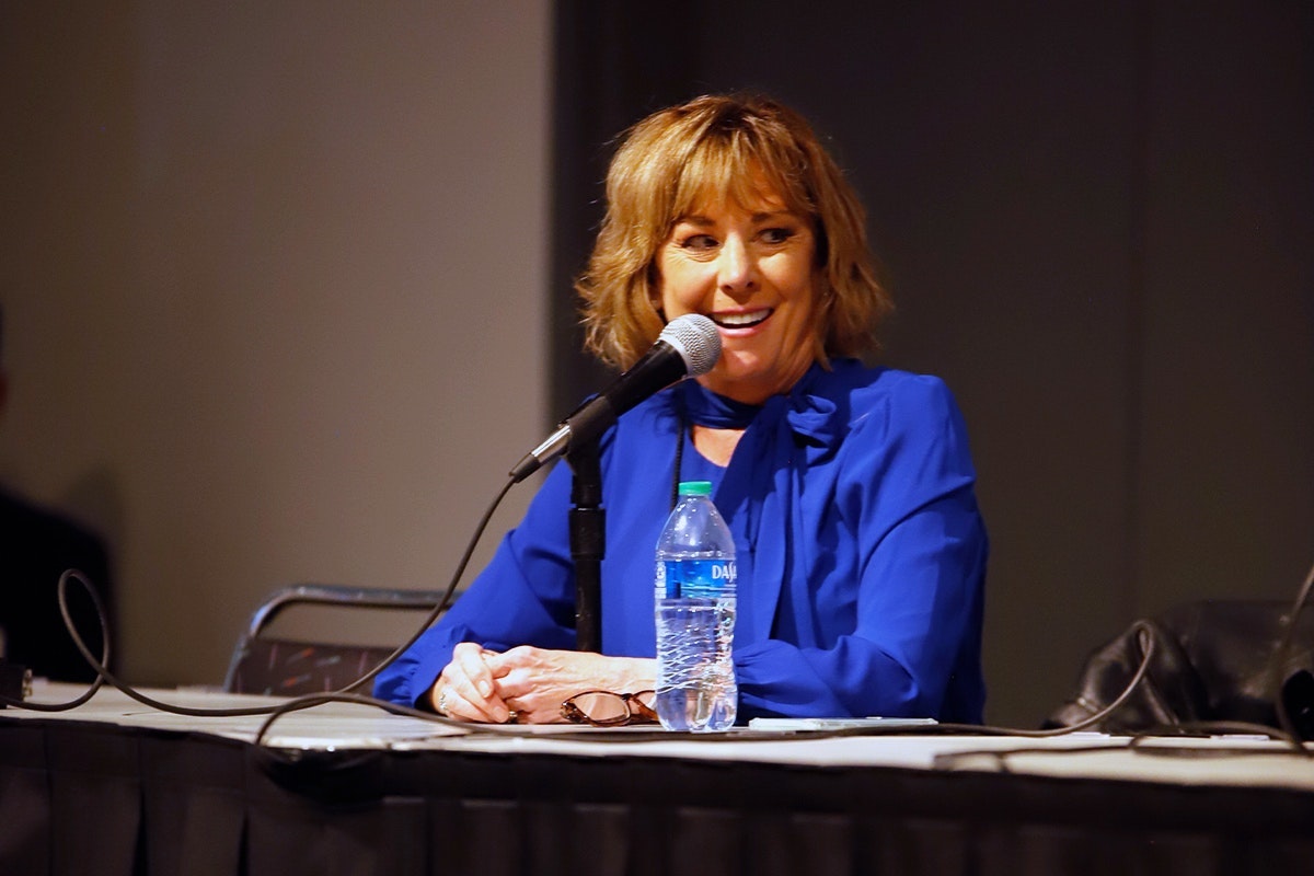 Paige O'Hara smiles while wearing a blue shirt and speaking into a microphone