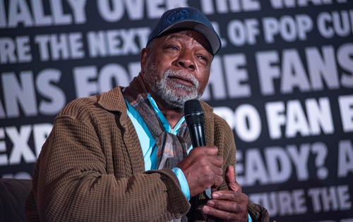 Carl Weathers listening to a fan ask a question; he is holding a microphone