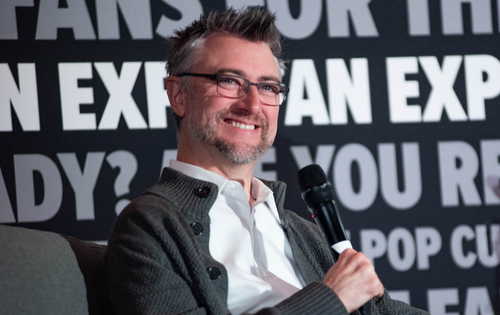 Sean Gunn smiling on stage and holding a microphone