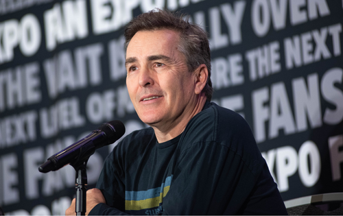 Nolan North smiling and talking into a microphone on stage