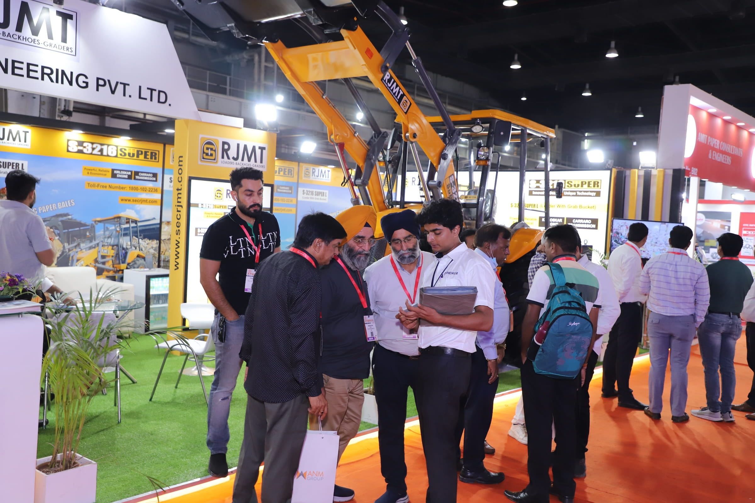 Attendees talking with exhibitors at a Paperex booth, with construction equipment visible in the background.
